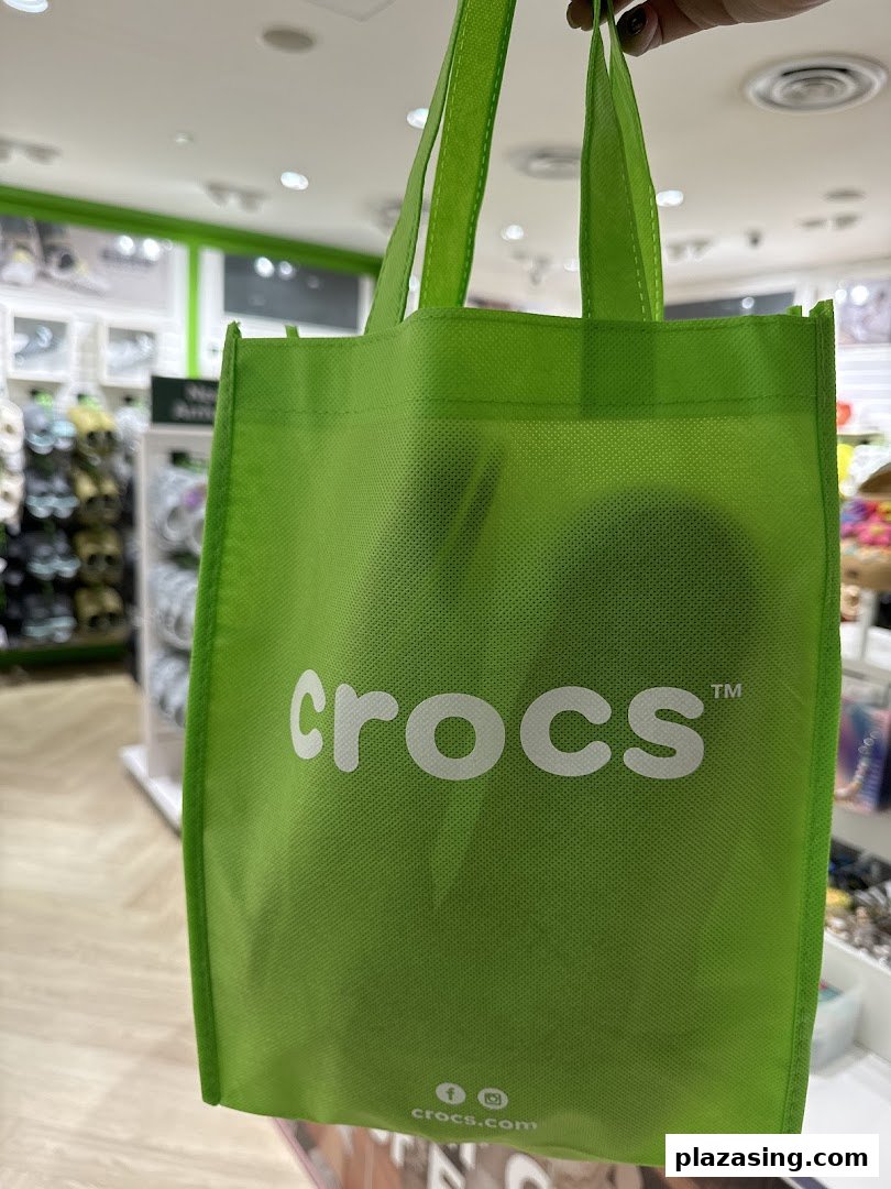 A bright green Crocs shopping bag held inside the Crocs store, showcasing the brand logo.