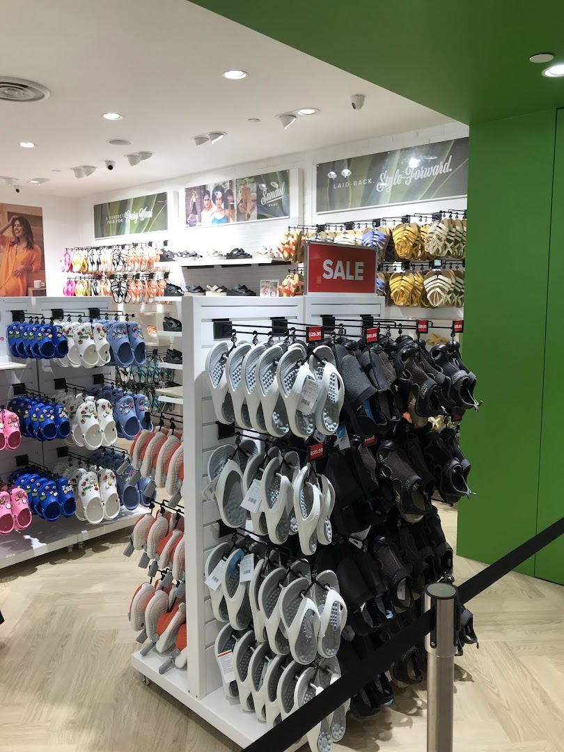 Interior view of a Crocs store showcasing a wide variety of colorful clogs, sandals, and flip-flops, including a sale section.