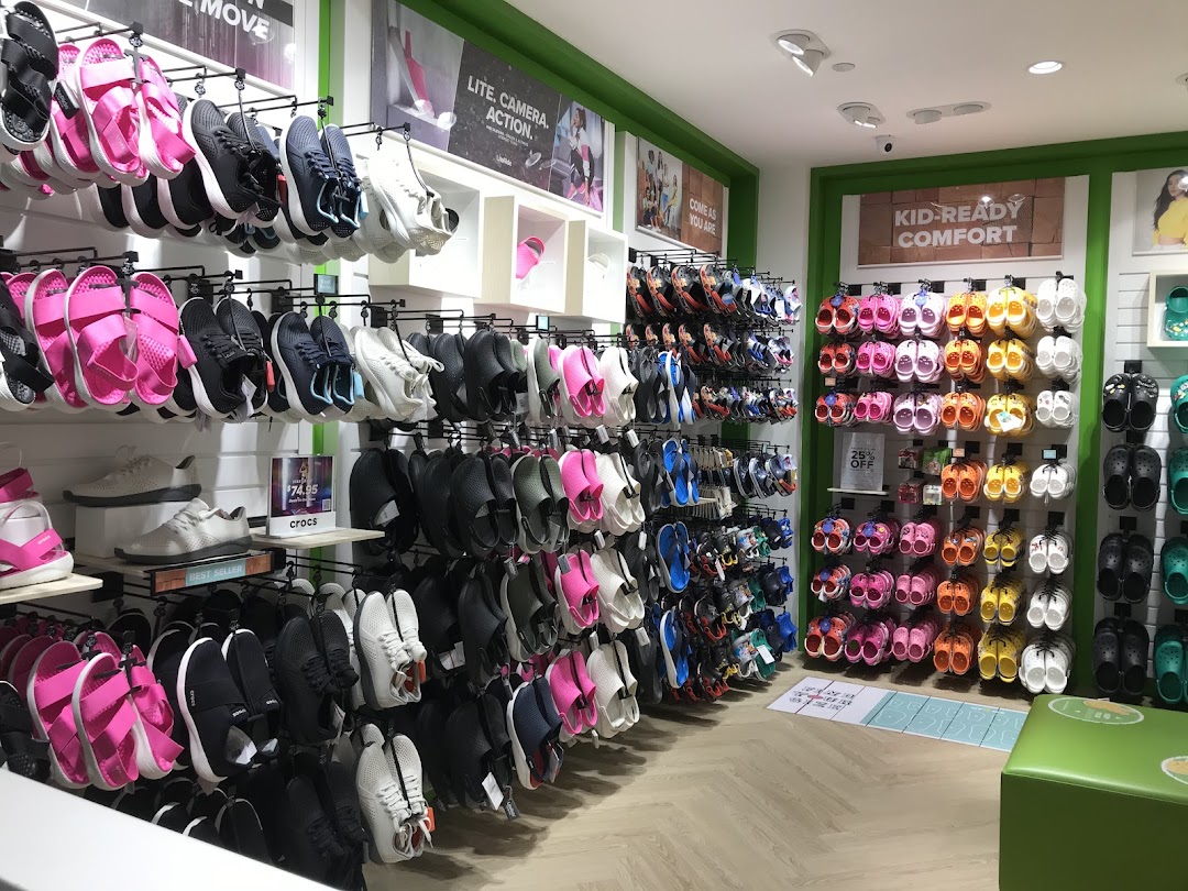 An interior view of a Crocs store showcasing a wide variety of colorful footwear, including clogs, sandals, and sneakers.