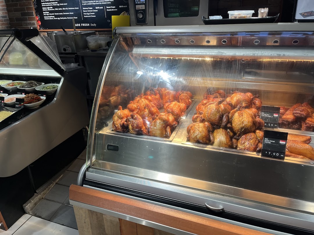 A deli counter at CS Fresh featuring roasted chickens, prepared salads, and a menu board.