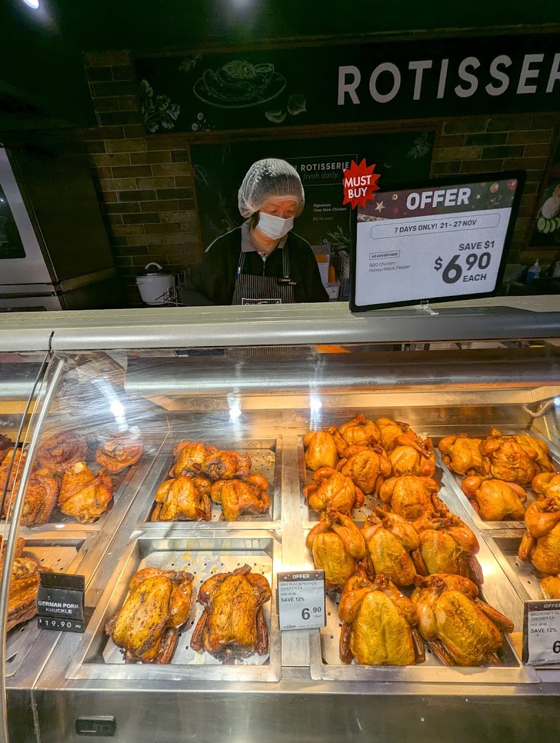 A staff member behind a display of freshly roasted rotisserie chickens and pork knuckles at CS Fresh.