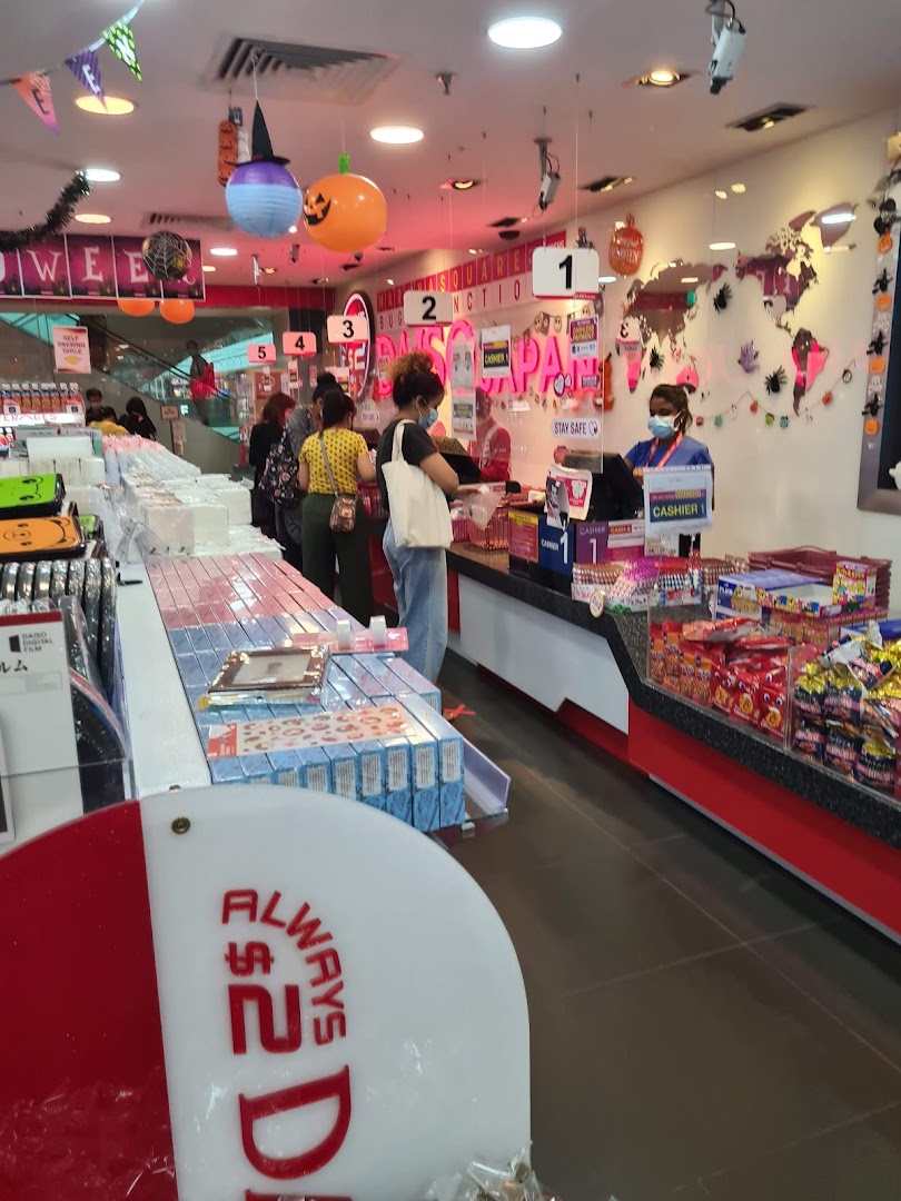 Customers queue at the checkout counter inside a Daiso store, featuring Halloween decorations and various products.