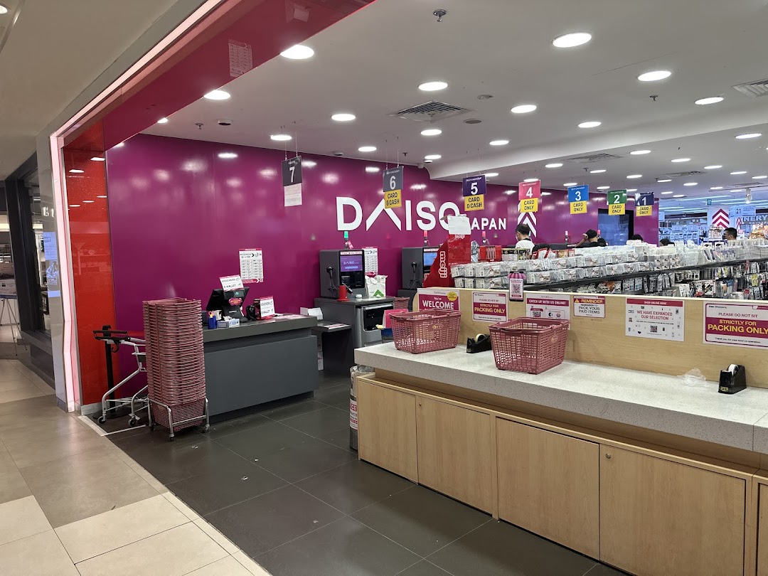 The vibrant pink entrance and checkout area of Daiso Japan, featuring multiple self-checkout counters.
