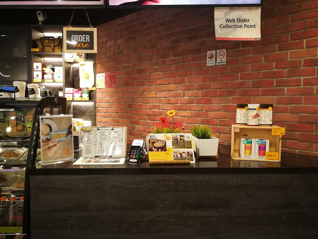 A well-lit cafe counter featuring coffee machines, a menu, and various products for sale.