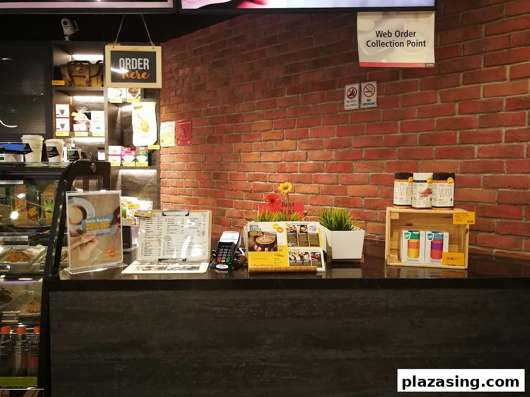 A well-lit cafe counter featuring coffee machines, a menu, and various products for sale.