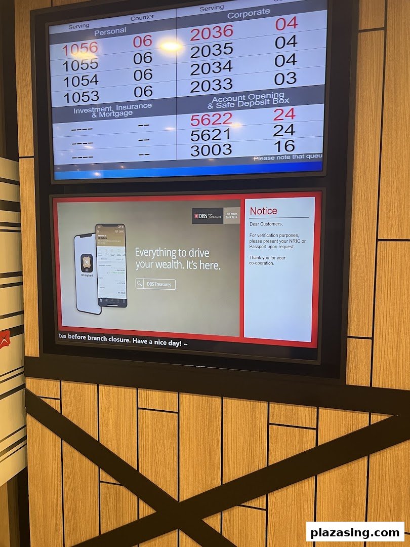 A digital queue management display and information screen inside a DBS bank branch.