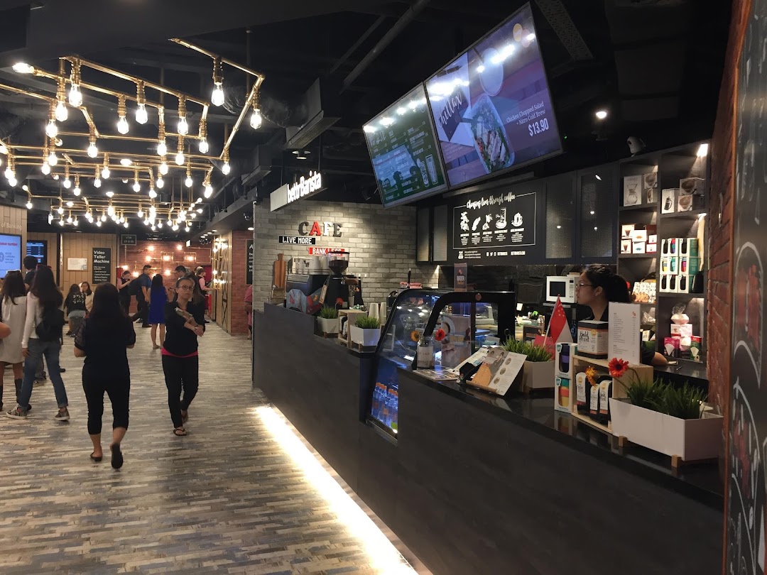 An interior view of a modern bank branch featuring a cafe counter, digital menus, and unique overhead lighting.