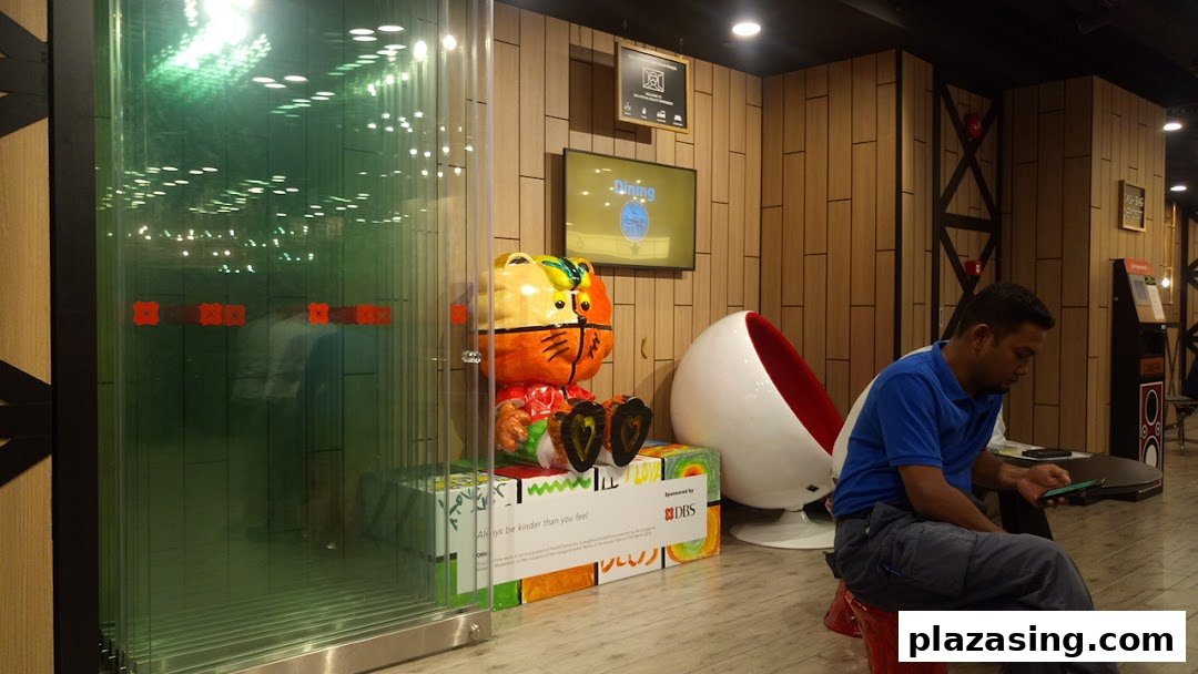 Interior view of DBS Plaza Singapura branch, featuring a colorful tiger statue, digital screens, and a customer.