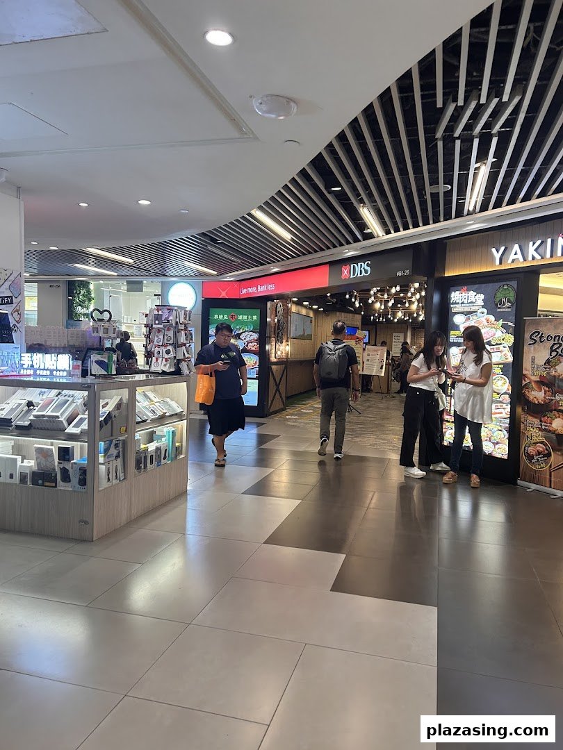 The entrance of DBS Plaza Singapura Branch is visible, with shoppers passing by and a nearby restaurant.