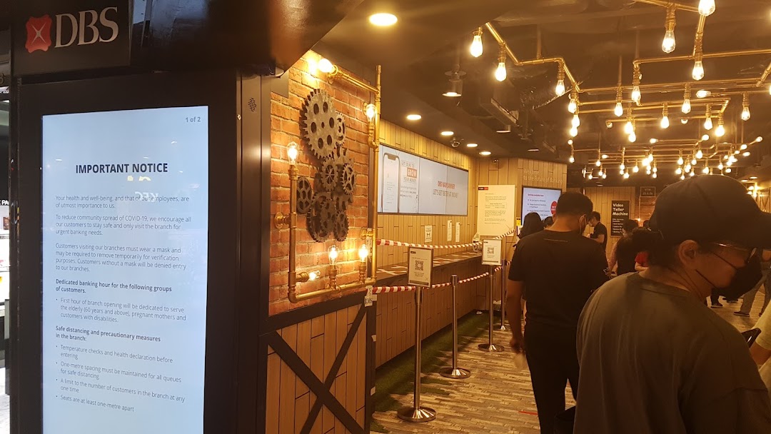 Interior view of a modern DBS bank branch with customers queuing and a digital notice board.