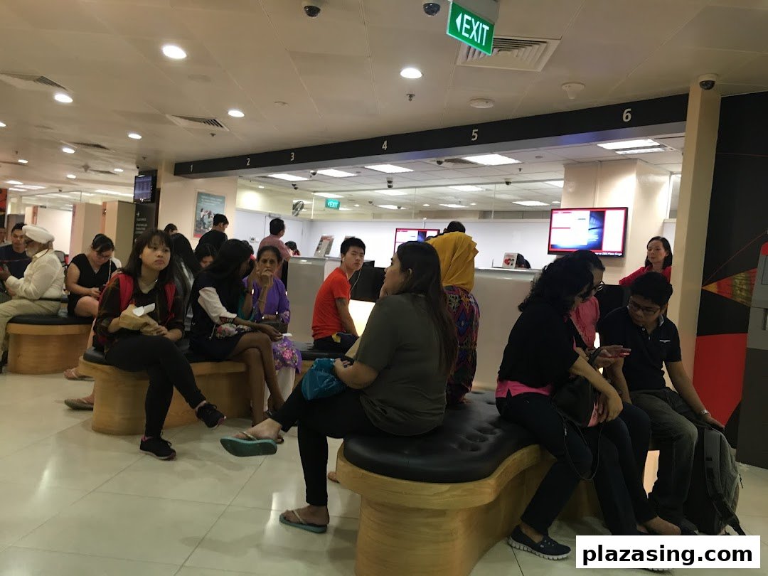 Customers wait in a spacious, well-lit service center with multiple counters and an exit sign visible.