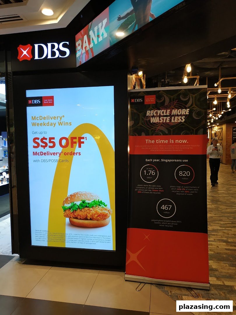 The entrance of DBS Bank at Plaza Singapura, featuring promotional displays for McDelivery and recycling initiatives.