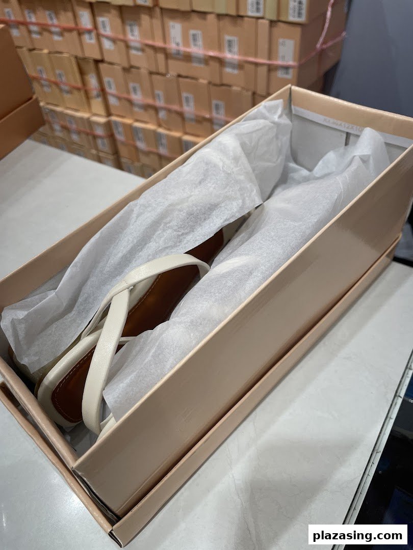 A pair of elegant white sandals in an open shoebox, surrounded by stacked inventory boxes.