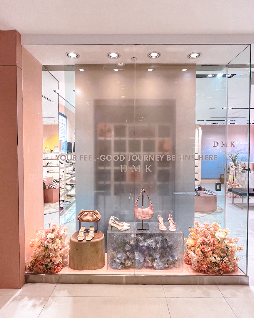 The DMK shopfront features a stylish display of shoes and bags, adorned with floral arrangements.