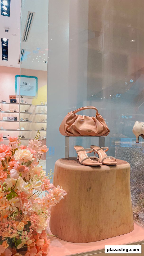 A stylish DMK shop window display featuring a peach handbag, sparkling heels, and floral decor.