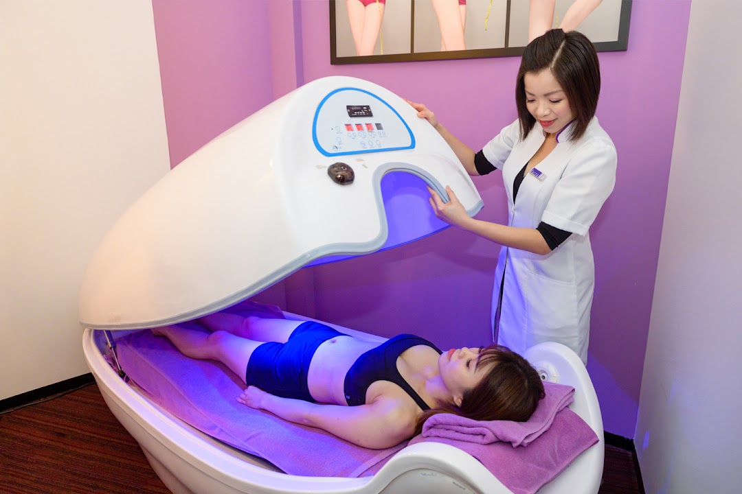 A staff member assists a client undergoing a lower body slimming treatment in a specialized pod.