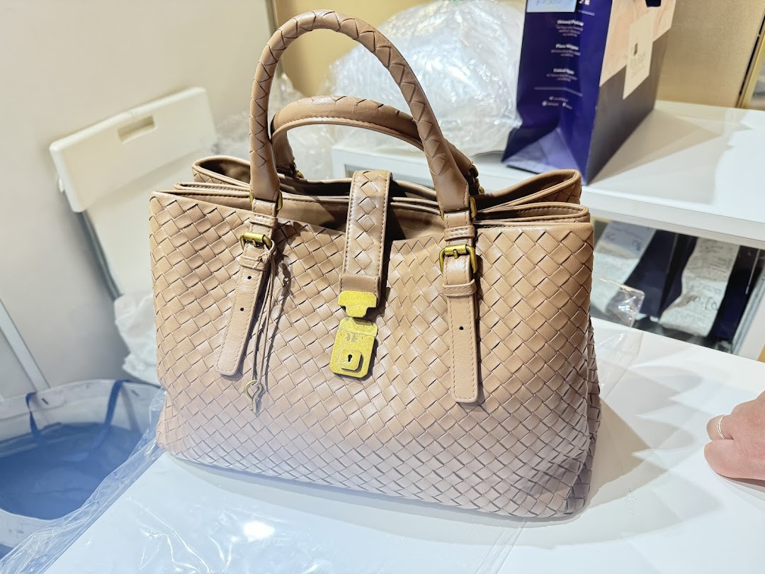 A close-up of a light brown woven leather handbag with a gold-tone lock and braided handles.