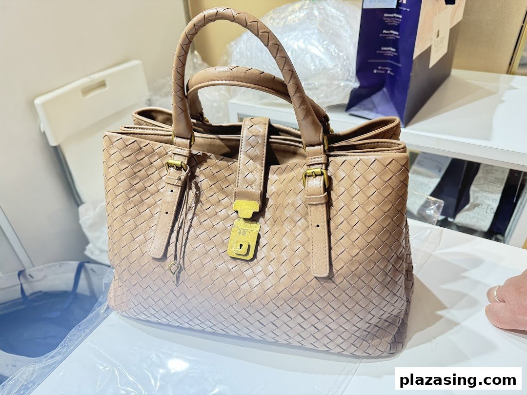 A close-up of a light brown woven leather handbag with a gold-tone lock and braided handles.