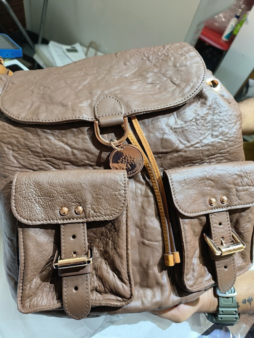 Close-up of a stylish brown leather backpack with front pockets and a brand charm.