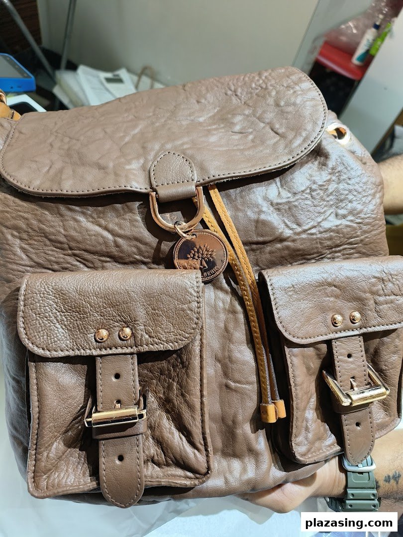 Close-up of a stylish brown leather backpack with front pockets and a brand charm.