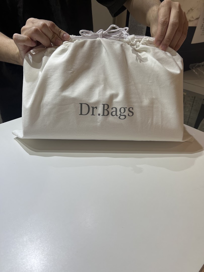 Hands holding a white dust bag with the 'Dr.Bags' logo on a white surface.