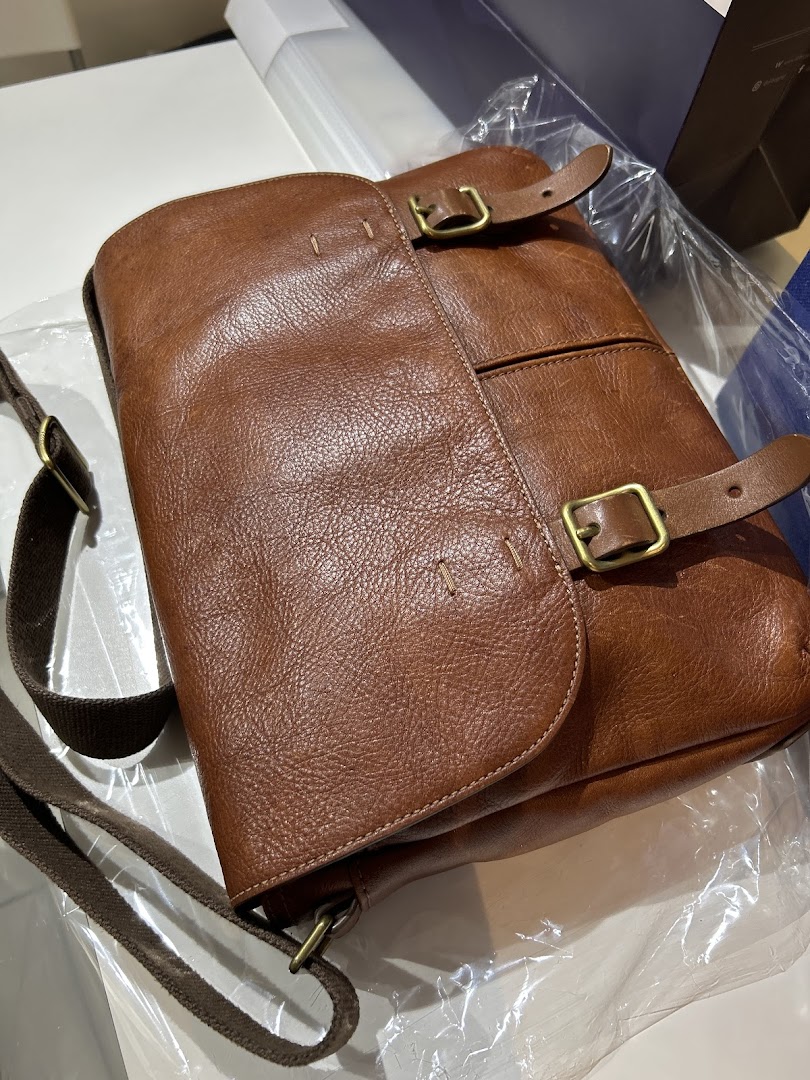 A close-up of a stylish brown leather messenger bag with buckle details.