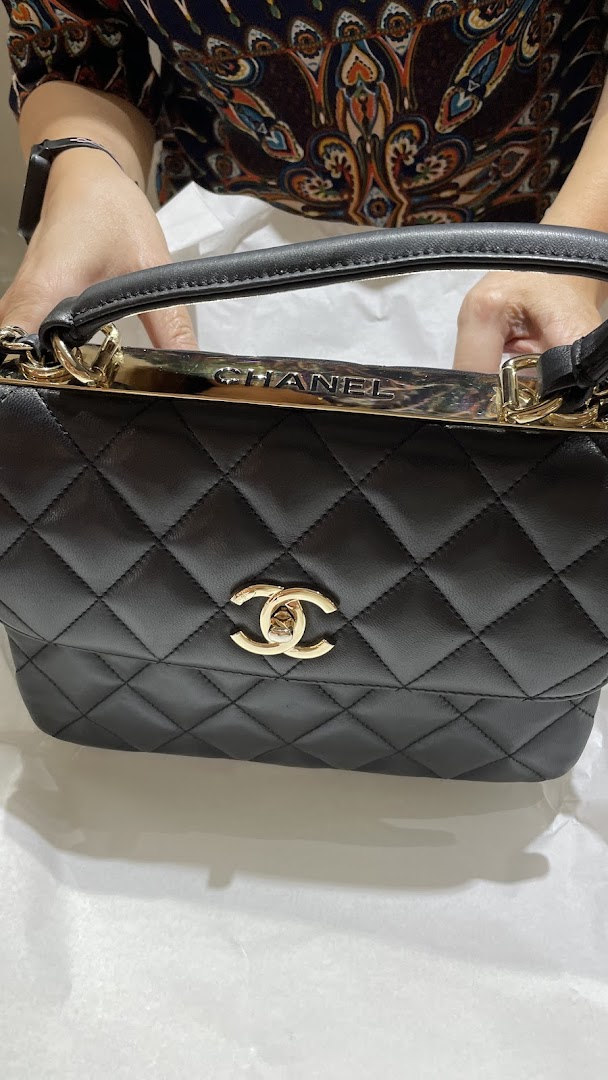 A person holding a black quilted Chanel handbag with gold hardware and logo.