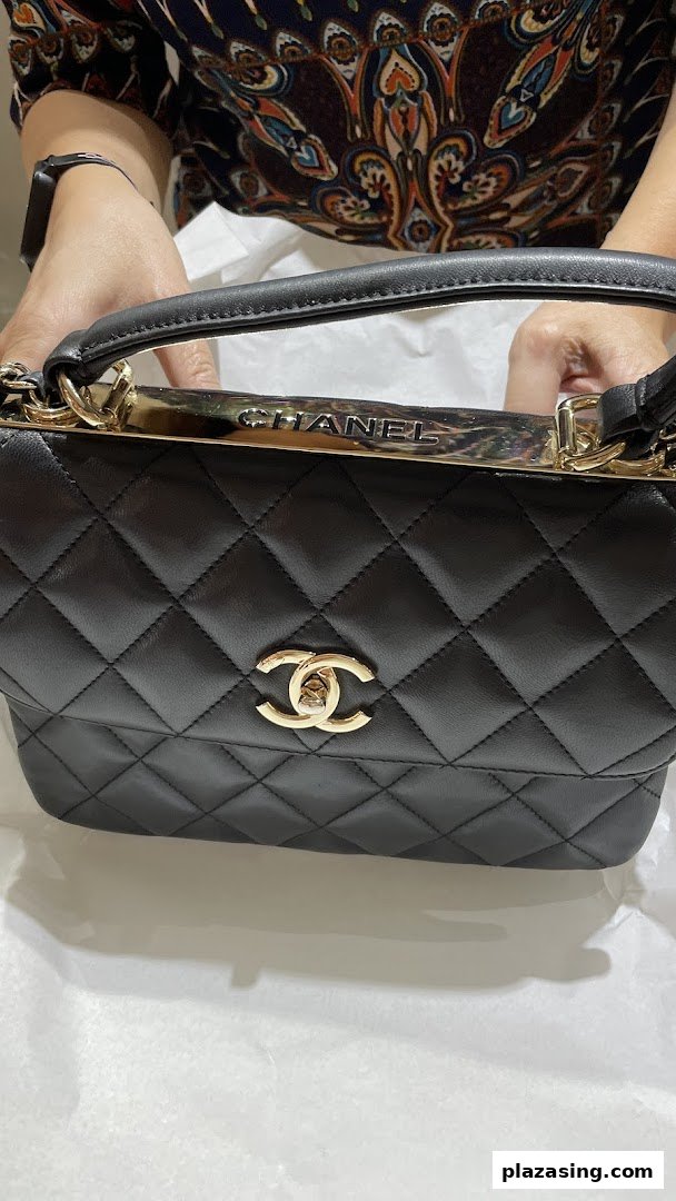 A person holding a black quilted Chanel handbag with gold hardware and logo.