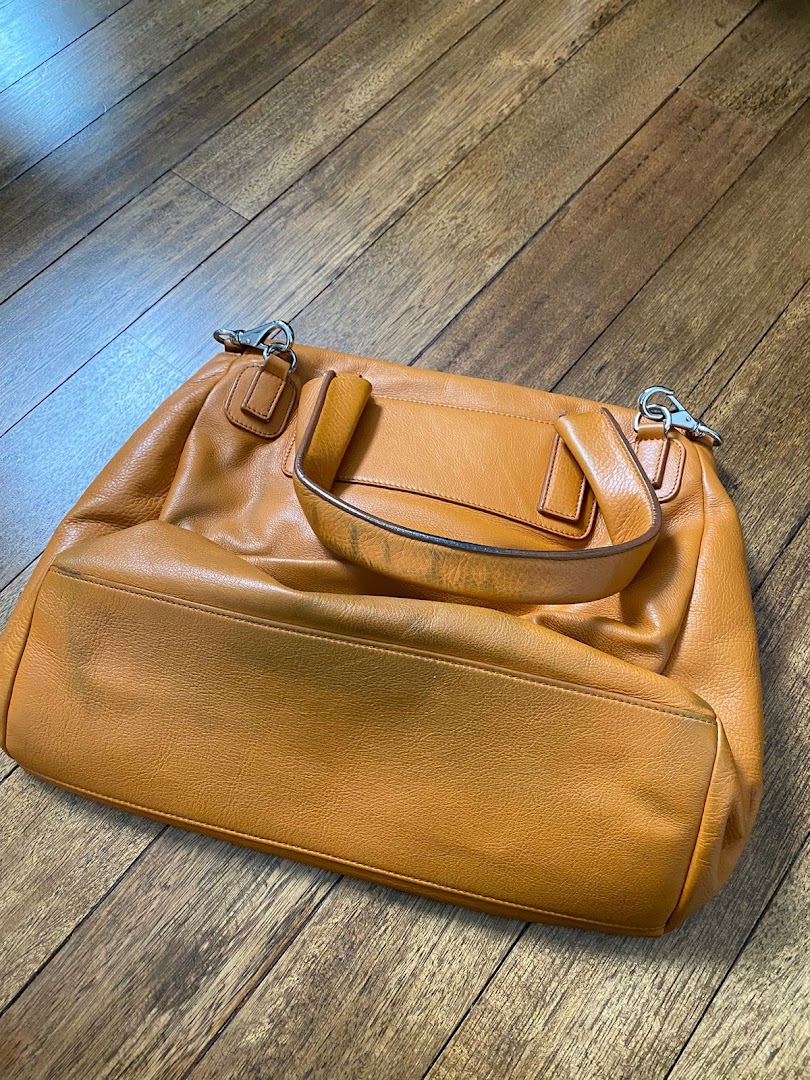 A stylish orange leather handbag displayed on a wooden floor.