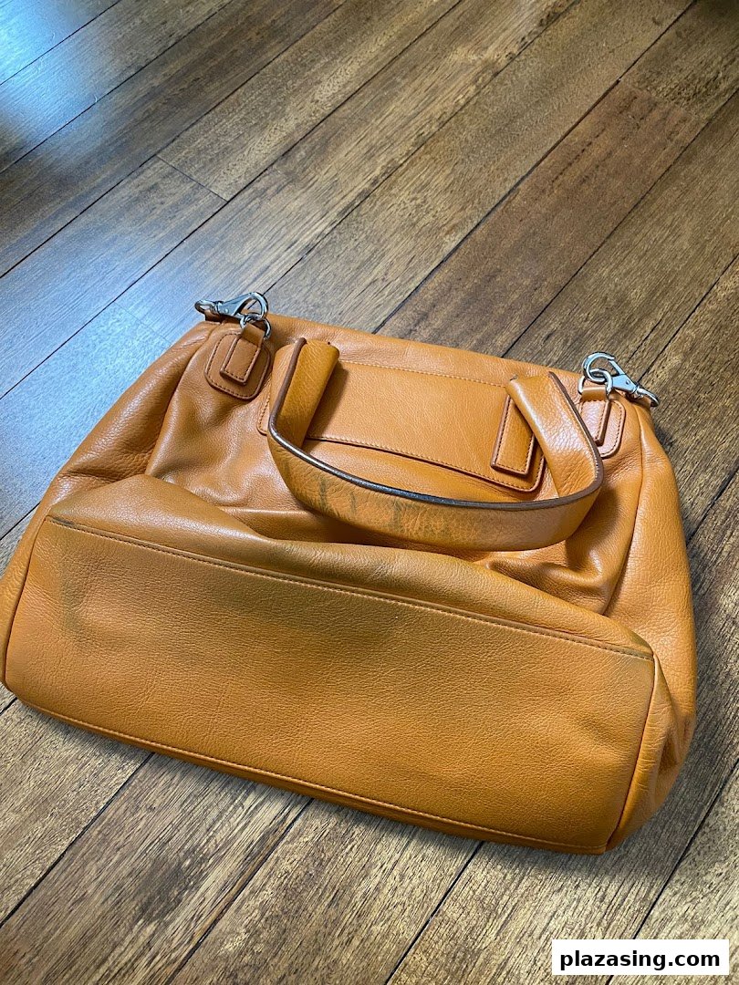 A stylish orange leather handbag displayed on a wooden floor.