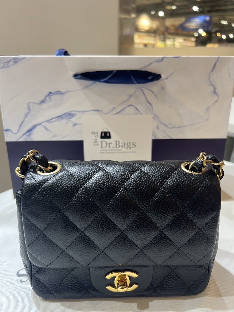 A black quilted handbag with gold hardware in front of a Dr.Bags shopping bag.