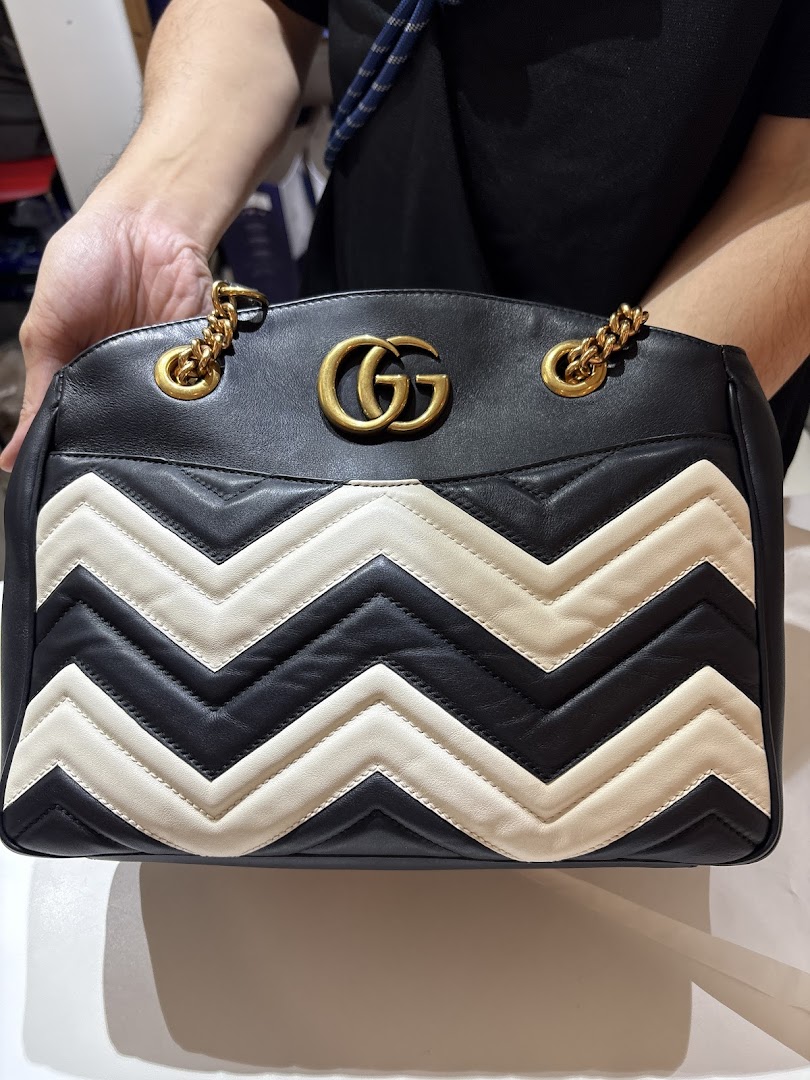 A person holds a black and white quilted handbag with a prominent gold logo.