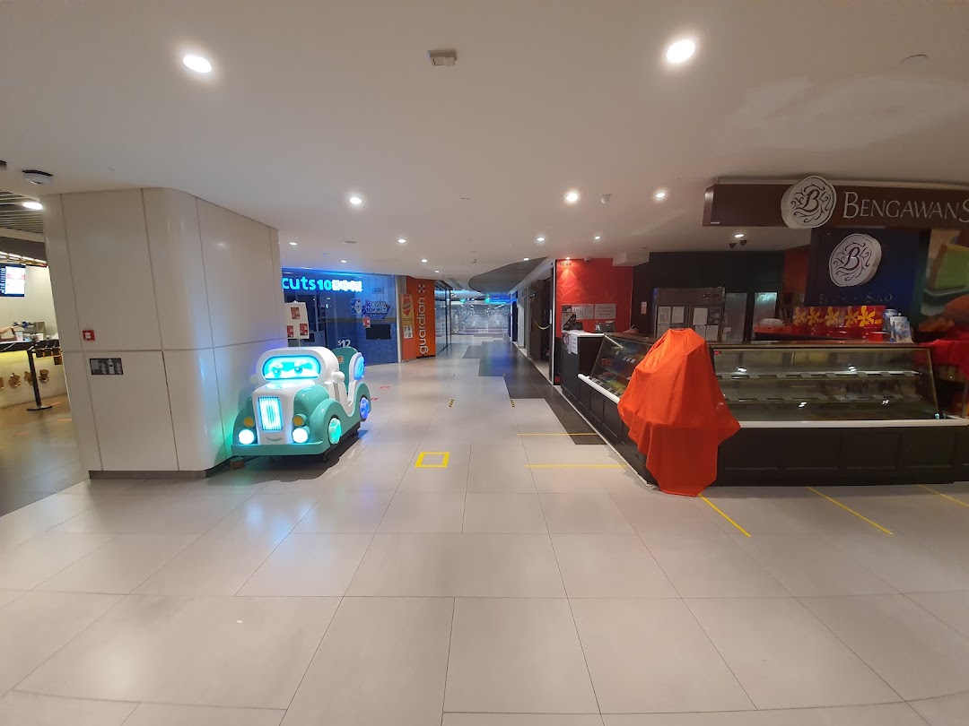 A bright mall corridor featuring shop fronts, a children's ride, and display cases.