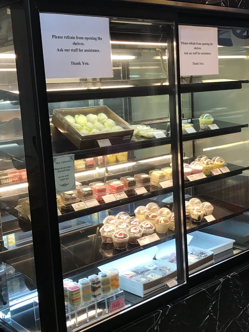 A brightly lit display case showcasing a variety of cakes, pastries, and desserts.