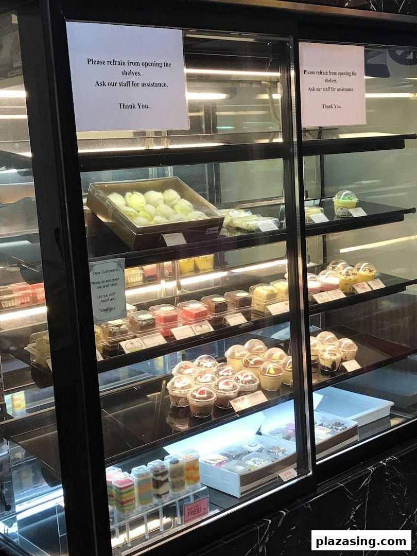 A brightly lit display case showcasing a variety of cakes, pastries, and desserts.
