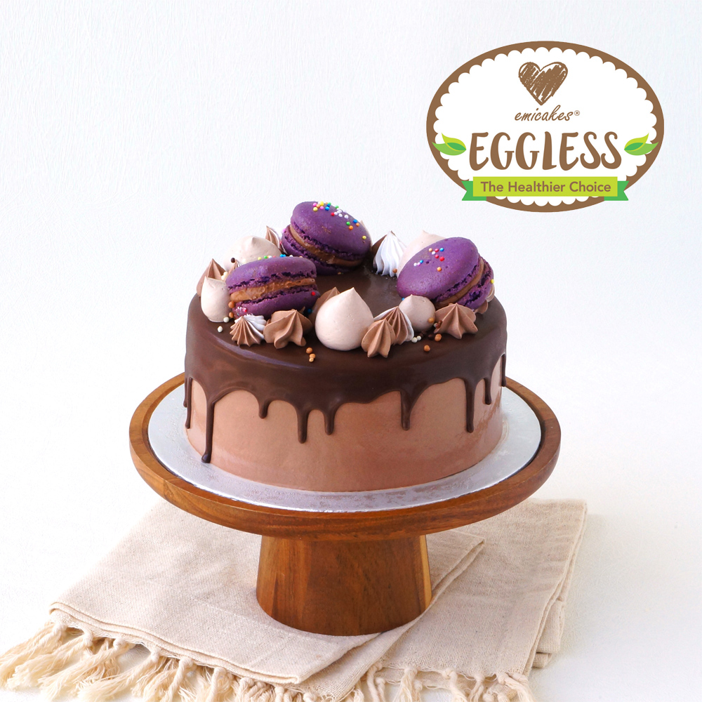 A beautifully decorated chocolate cake with purple macarons and meringue on a wooden stand.