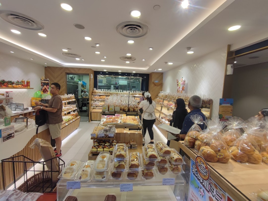 Customers browse a wide selection of freshly baked bread and pastries inside a bright, modern bakery.