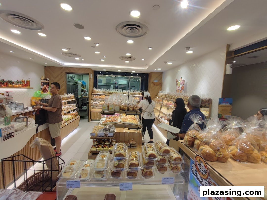 Customers browse a wide selection of freshly baked bread and pastries inside a bright, modern bakery.