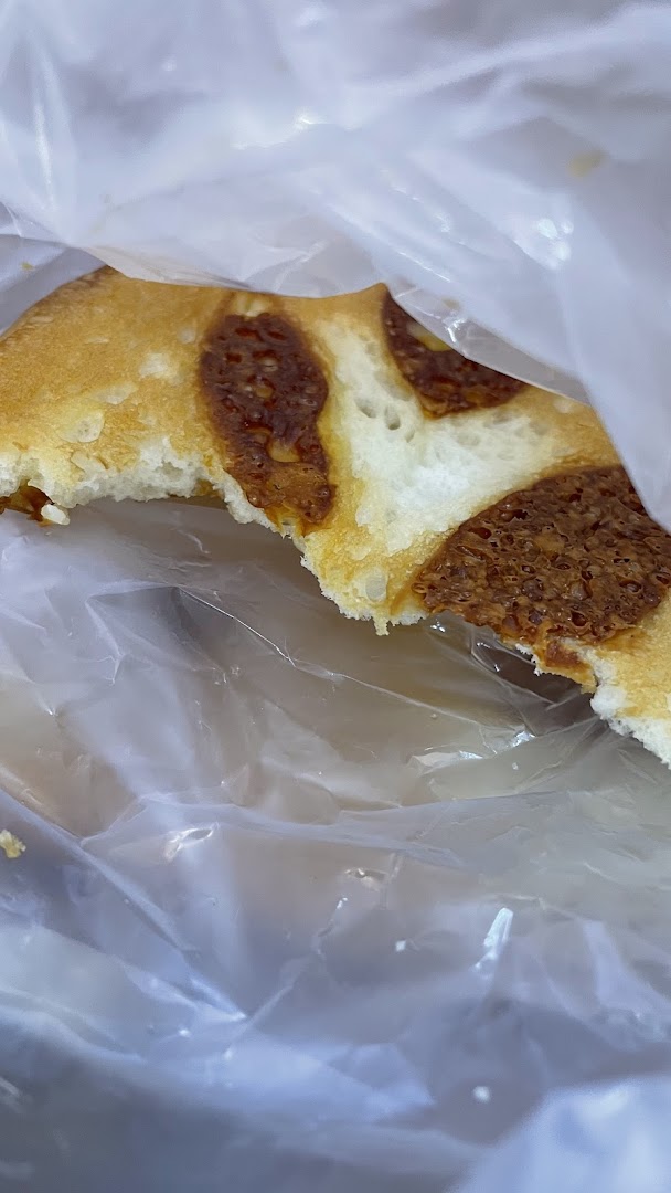 A close-up of a delicious baked good with a savory topping, partially wrapped in plastic.