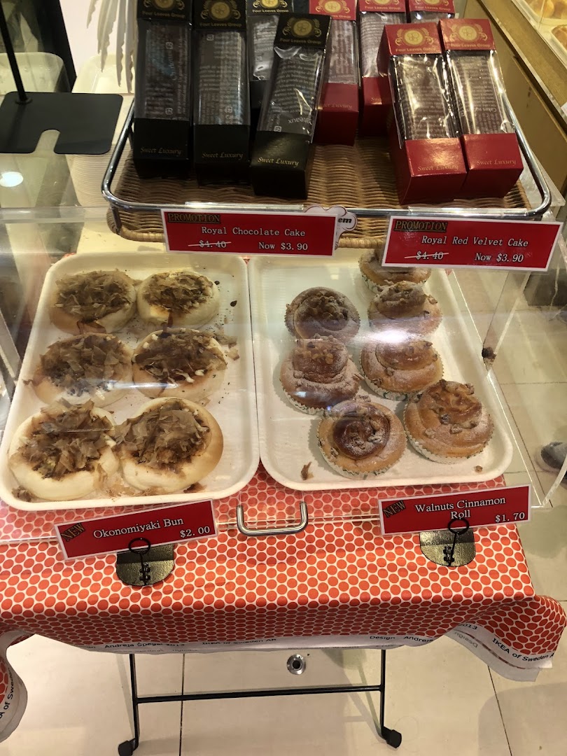A display case showcasing various baked goods like Okonomiyaki buns, cinnamon rolls, and promotional cakes with prices.