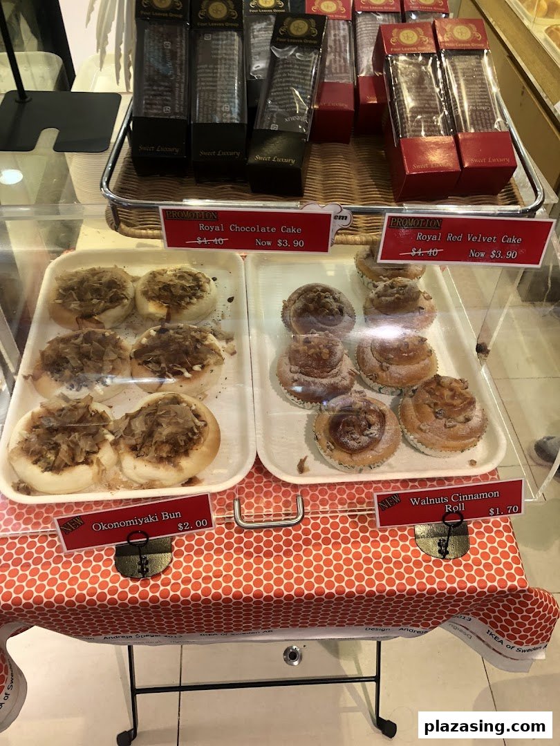 A display case showcasing various baked goods like Okonomiyaki buns, cinnamon rolls, and promotional cakes with prices.