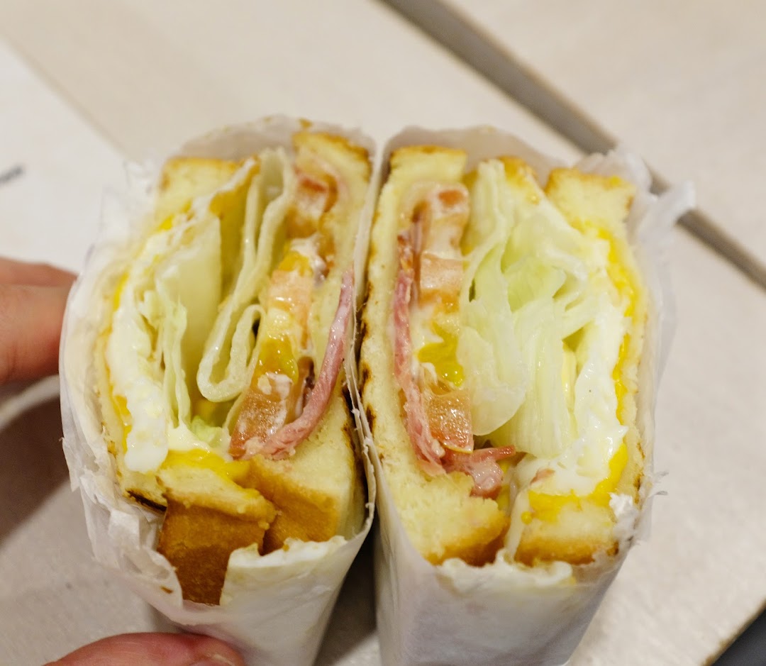 A close-up of a freshly made sandwich, cut in half, revealing layers of lettuce, ham, and egg.
