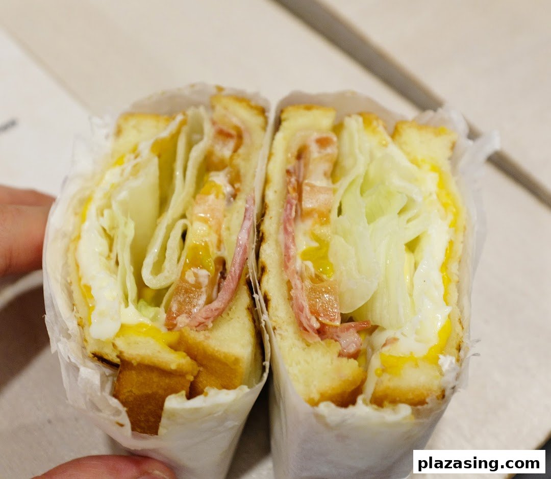 A close-up of a freshly made sandwich, cut in half, revealing layers of lettuce, ham, and egg.