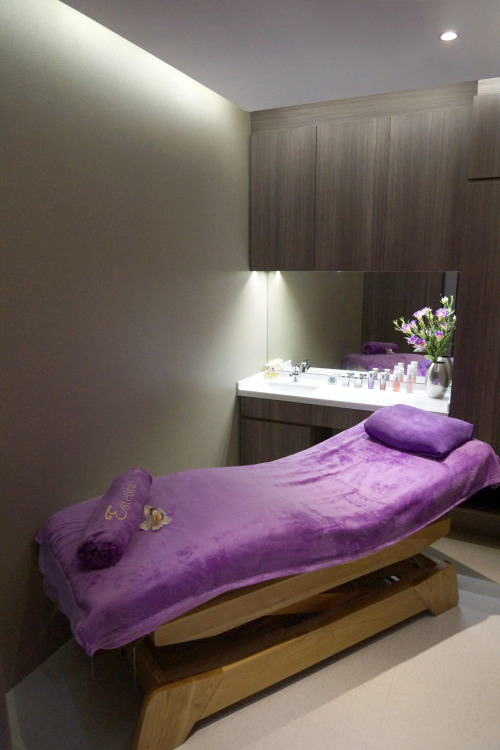 A serene spa treatment room with a purple-covered bed and a vanity area.