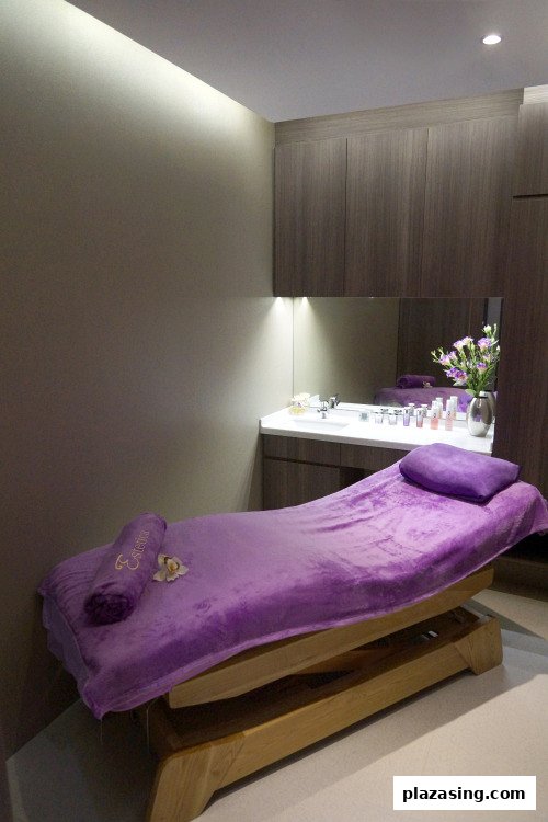 A serene spa treatment room with a purple-covered bed and a vanity area.