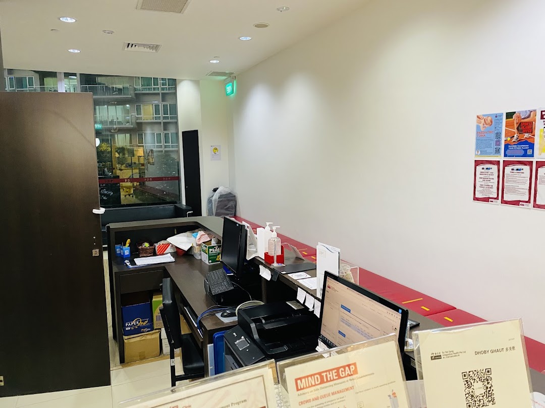 An interior view of a clinic reception area with a counter, computers, and a red waiting bench.