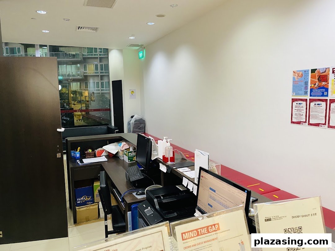 An interior view of a clinic reception area with a counter, computers, and a red waiting bench.