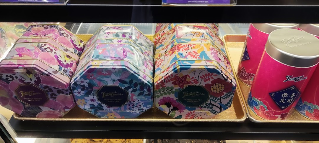 Colorful Famous Amos cookie tins and festive cylindrical containers displayed in a retail case.