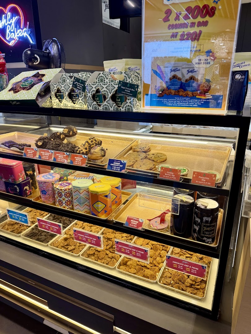 A vibrant display case showcasing freshly baked Famous Amos cookies, muffins, and gift tins, with a promotional offer visible.
