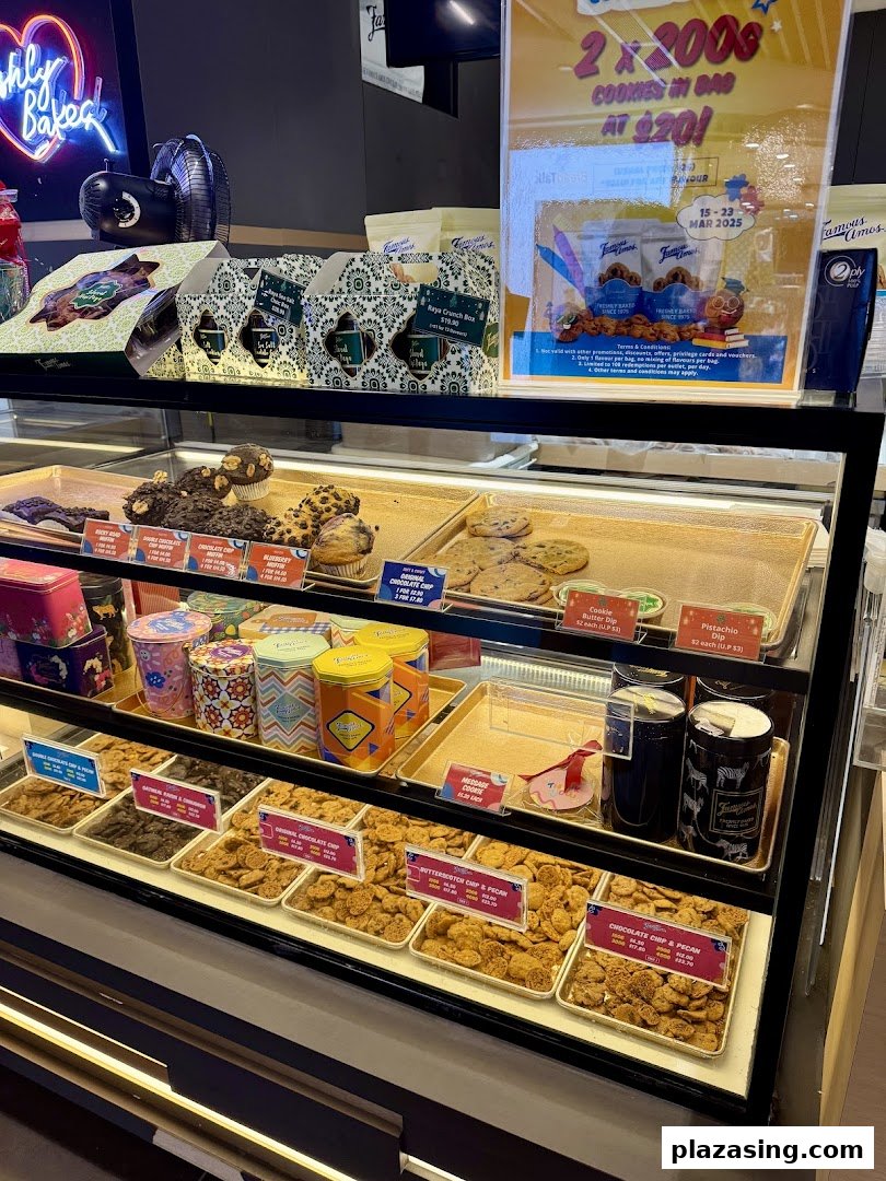 A vibrant display case showcasing freshly baked Famous Amos cookies, muffins, and gift tins, with a promotional offer visible.
